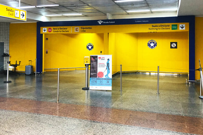 Foto da alfândega vazia no aeroporto de Guarulhos. As paredes são pintadas de amarelo e tem o símbolo da Polícia Federal