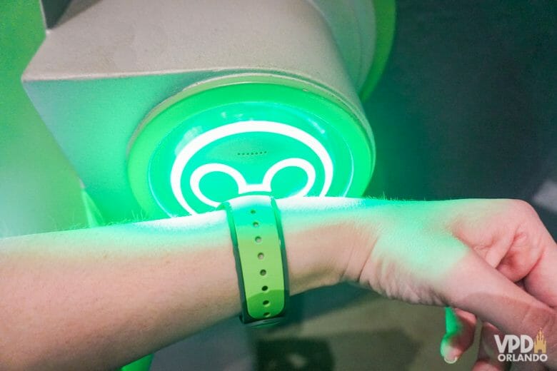 Foto de uma hóspede de um hotel da Disney escaneando a MagicBand verde na entrada de uma atração. A entrada tem um visor em forma de Mickey, que fica verde ao escanear a MagicBand. 