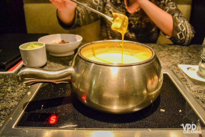 Se for viajar no inverno, aproveite o clima friozinho para comer um fondue no Melting Pot. :) Foto da panela de fondue de queijo; a Bia está segurando o pedaço de pão e o queijo derretido está escorrendo.