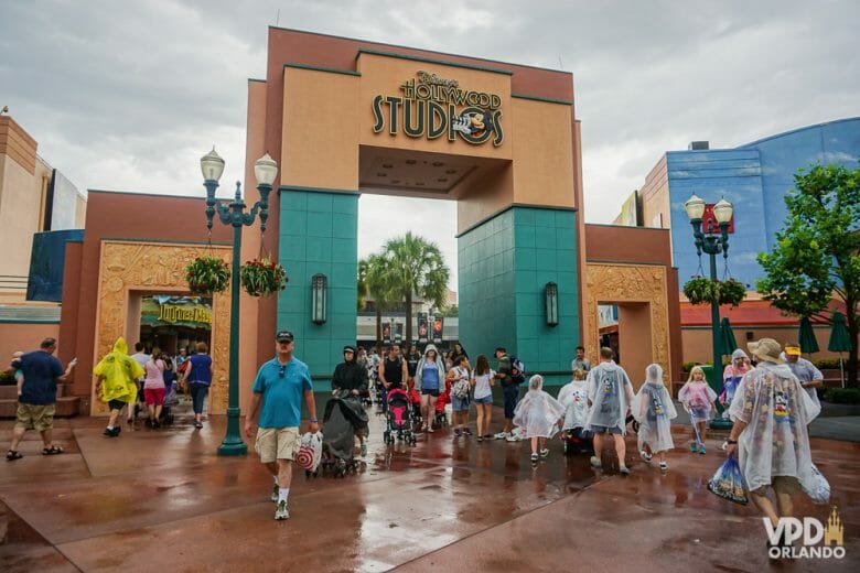 Clima chuvoso no Hollywood Studios. A foto mostra a entrada de uma das áreas do parque, o céu nublado e diversos visitantes com capas de chuva. 