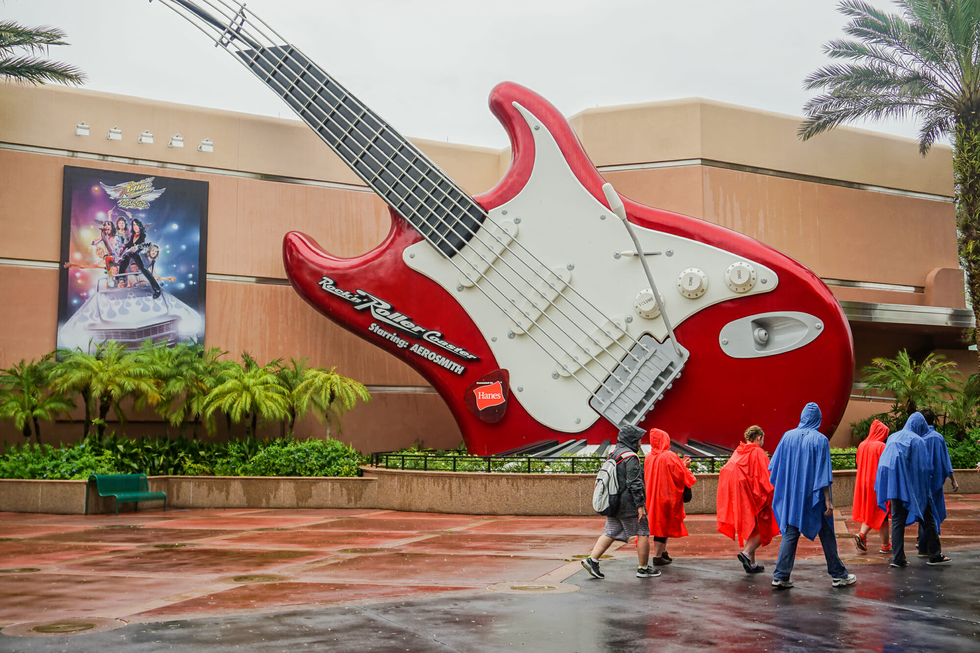 Foto da guitarra da atração Rock 'n' Roller Coaster, do Hollywood Studios, em um dia nublado. Os visitantes que estão passando vestem capas de chuva.