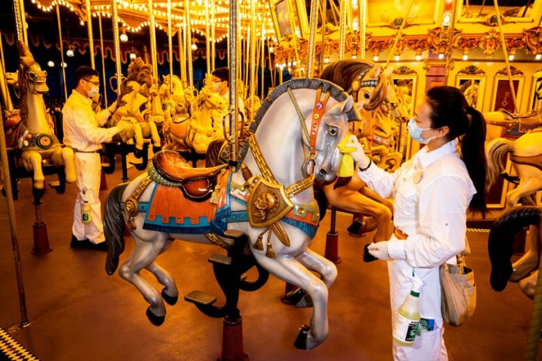 Foto de uma funcionária de máscara fazendo a limpeza do cavalo do carrossel da Disney de Hong Kong 