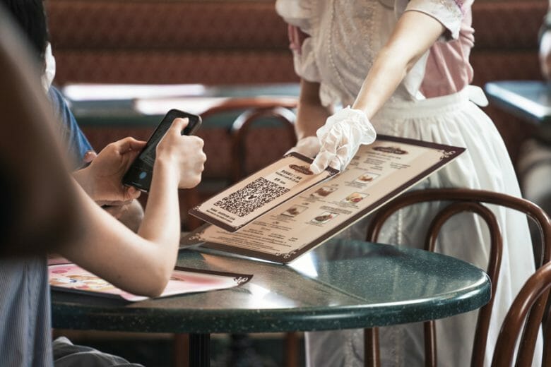 Foto de uma funcionária de luvas nas mãos entregando um cardápio a um visitante na Disney de Hong Kong