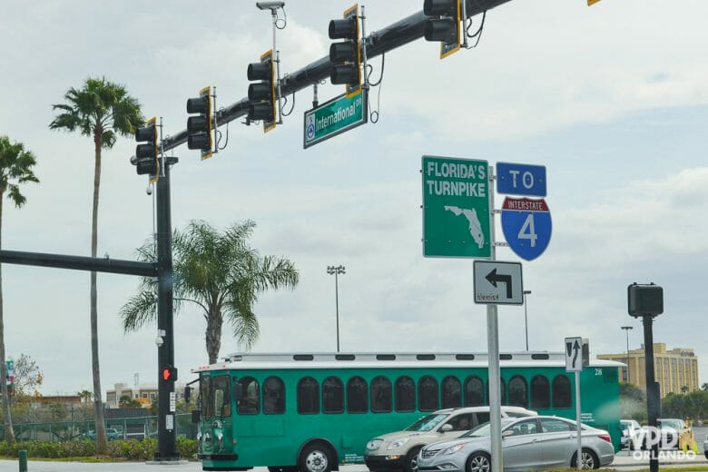 Imagem de uma rua em Orlando, com ônibus e carros parados no semáforo. As placas indicam o caminho para as rodovias.