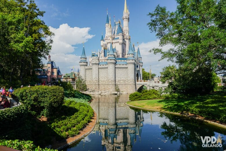 99% das pessoas querem ver este castelo, mas quais outros parques você quer ver em Orlando? Foto do castelo da Cinderela no Magic Kingdom, com árvores ao redor, o lago em frente e o céu azul ao fundo 