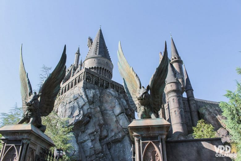 Foto do castelo de Hogwarts, que fica em um dos parques da Universal, o Islands of Adventure, com o céu azul ao fundo e alguns visitantes entrando. 