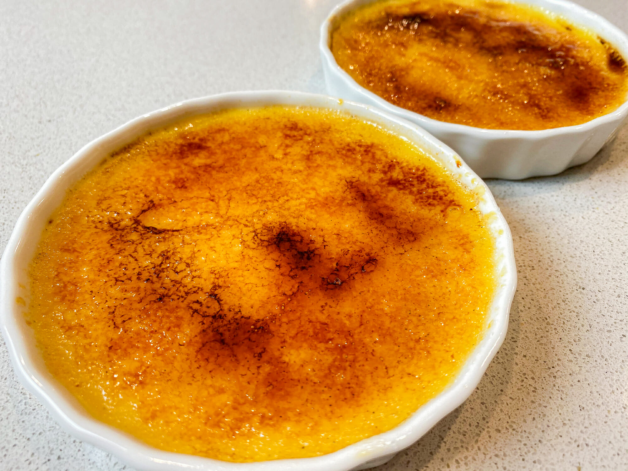 Foto de dois potinhos com crème brûlée, com a característica cobertura de açúcar queimado.