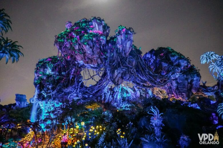 A área de Pandora no Animal Kingdom fica ainda mais incrível à noite! Foto das rochas na decoração de Pandora à noite, iluminadas em azul escuro com luzinhas coloridas mais abaixo 