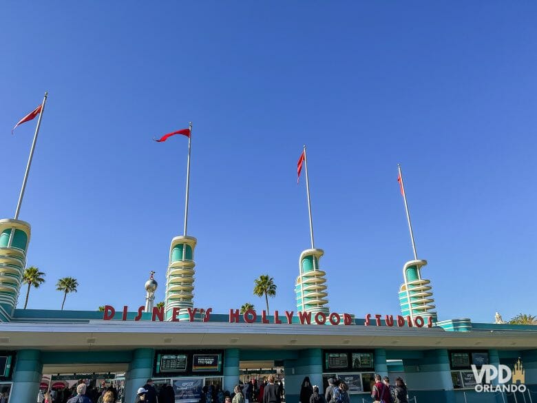 Foto da entrada do Hollywood Studios, que é pintada de azul com o nome do parque acima em vermelho. 