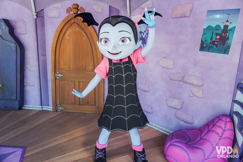 Os personagens de Disney Junior ficam ali encontrando os visitantes. Foto da personagem Vampirina, no Hollywood Studios, acenando para visitantes em uma casa com paredes roxas. 