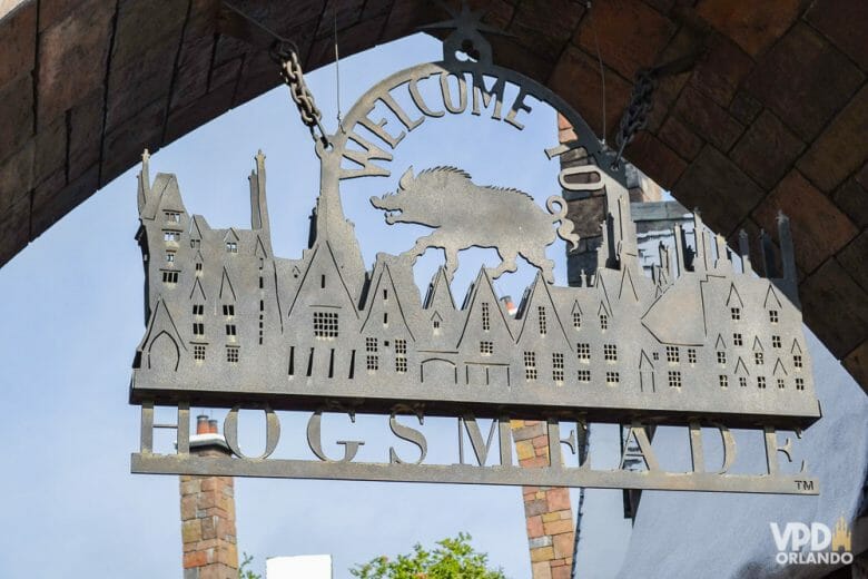 Foto da placa na entrada da vila de Hogsmeade no Islands of Adventure, que mostra um javali, as construções da vila e diz "welcome to Hogsmeade"