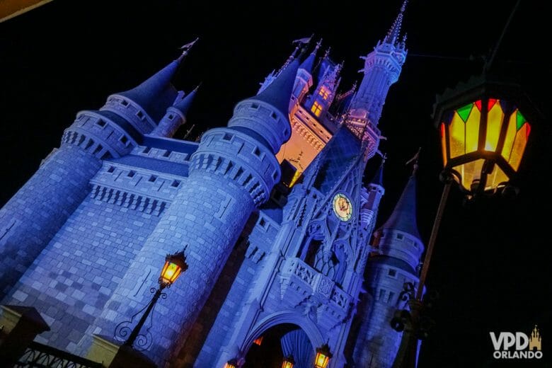 Foto do castelo da Cinderela no Magic Kingdom, um dos parques que todo mundo quer visitar! Ele está iluminado em azul e o céu noturno está ao fundo 