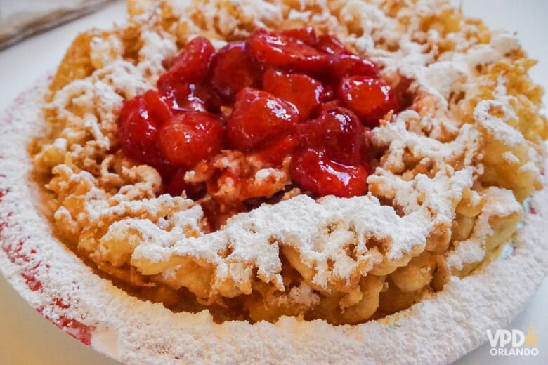 Foto do funnel cake do Magic Kingdom, uma massinha polvilhada de açúcar com calda de morango no centro. 