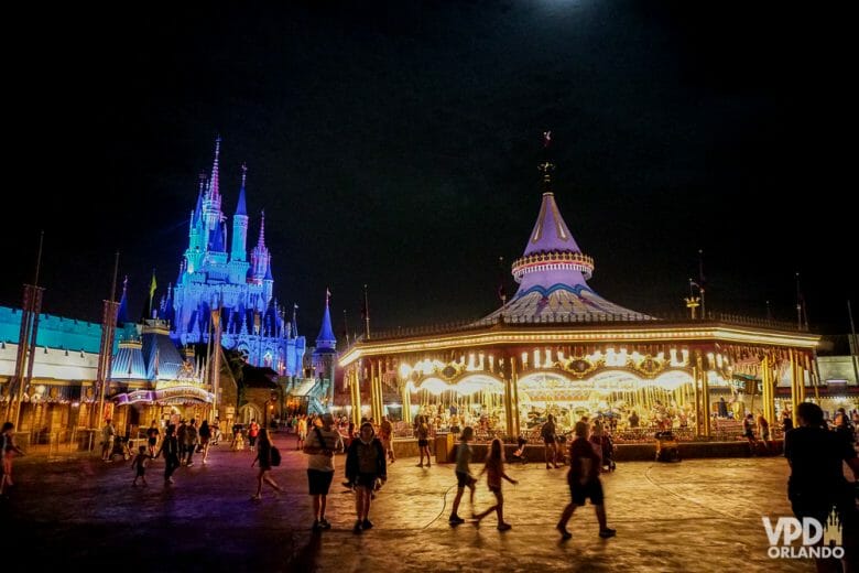 Foto da Fantasyland do Magic Kingdom à noite, com o carrossel iluminado e o castelo da Cinderela também iluminado ao fundo