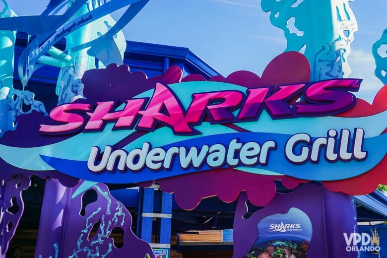 O Sharks Underwater Grill é o restaurante mais interessante do SeaWorld. Foto da entrada do restaurante Sharks Underwater Grill, com o título em rosa e branco sobre um fundo em tons de azul 