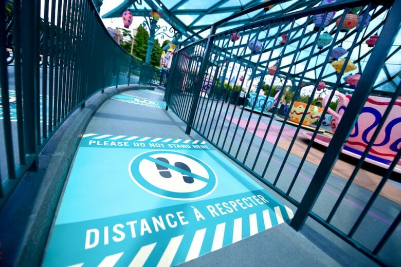 Foto dos sinais indicando a distância que deve ser mantida entre os visitantes no chão do parque na Disneyland de Paris. 