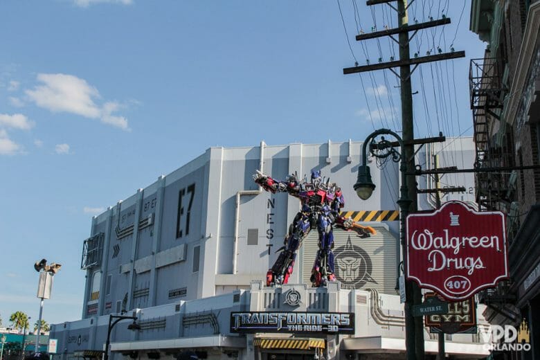 Foto na frente do simulador de Transformers na Universal Studios, com um dos robôs do filme em tamanho gigante acima da placa. 