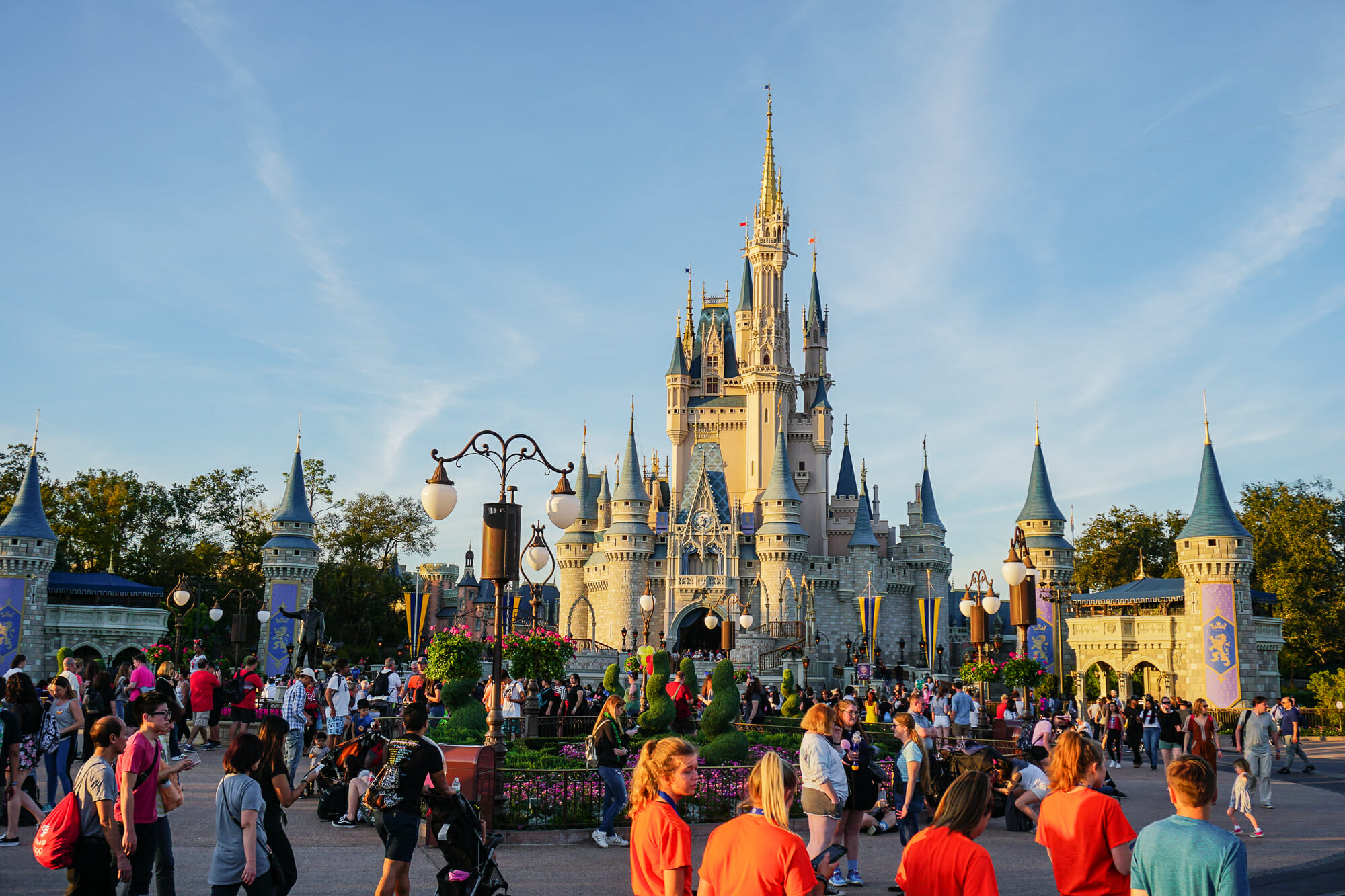 Foto do castelo da Cinderela do Magic Kingdom em um dia de céu azul, com muitos visitantes circulando pelo parque.