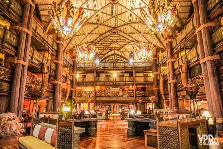 Recepção maravilhosa do Animal Kingdom Lodge. A imagem mostra o lobby do Animal Kingdom Lodge, um dos hotéis de luxo da Disney. A decoração é toda em madeira, com pilares, teto alto e lustres coloridos. 