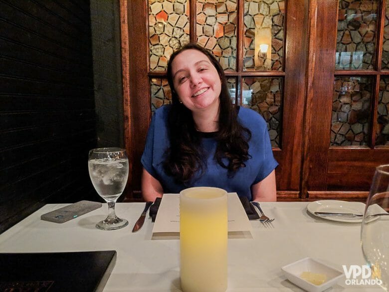 Uma experiência bem gostosa mas nada esnobe! Foto da Renata sentada à mesa do Chef's Table at the Edgewater, com uma taça de água ao seu lado e uma vela à sua frente 
