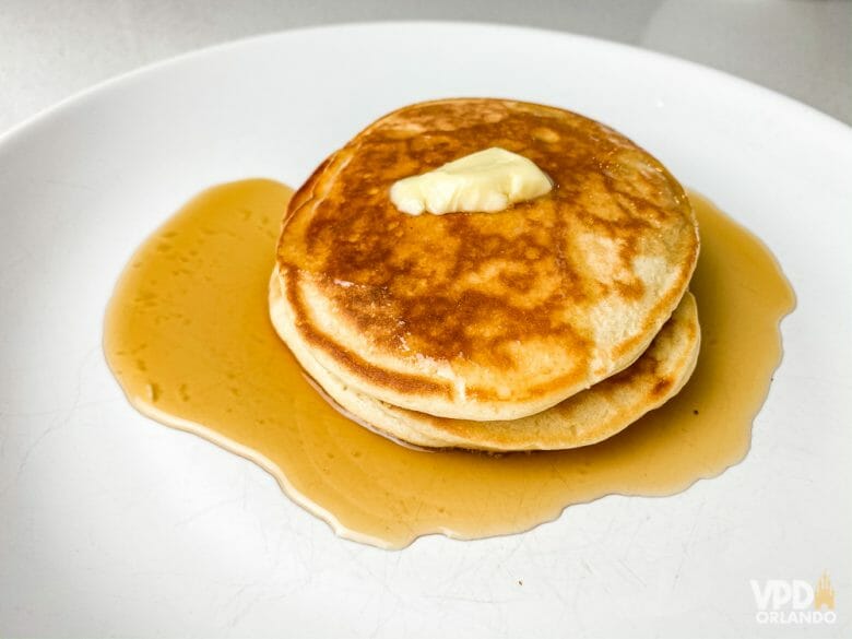 A panqueca americana é uma das melhores comidas de café da manhã! A imagem mostra um prato com duas panquecas americanas com um pouco de manteiga em cima e xarope de maple embaixo. 