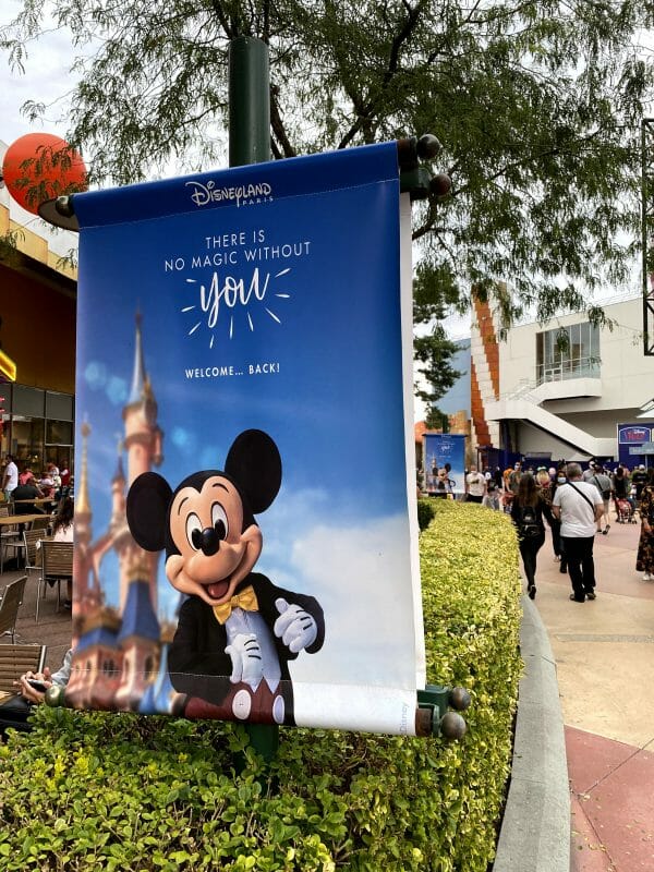 Imagem de um pôster na Disneyland Paris. O pôster mostra o Mickey de terno e gravata borboleta, com o castelo e o céu azul ao fundo. 