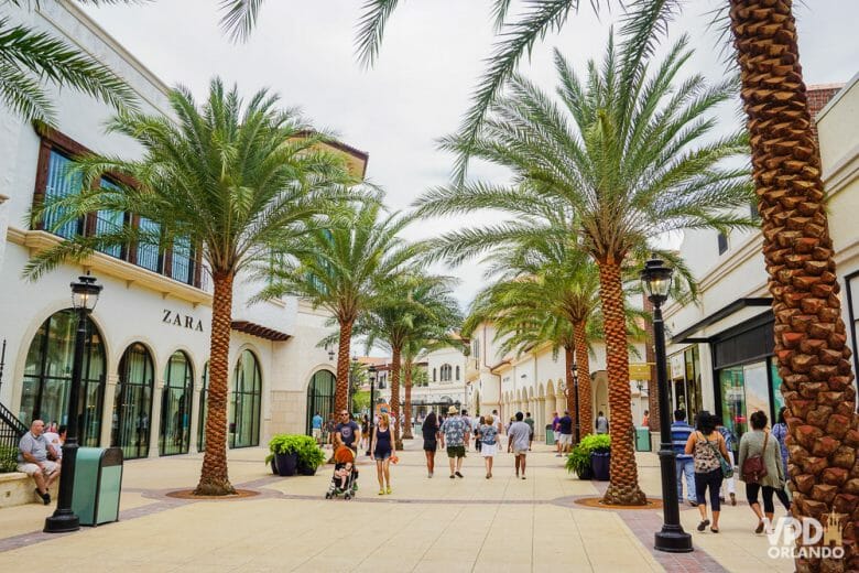 A área do Town Center parece até um outlet, de tantas lojas incríveis. Foto do centro de Disney Springs, rodeado de lojas, com palmeiras e visitantes passeando. 