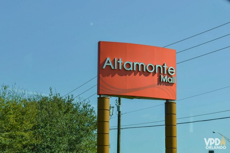 Um dos shoppings alternativos próximos a Orlando. Imagem da placa do Altamonte Mall em vermelho, com o céu azul e árvores ao fundo. 