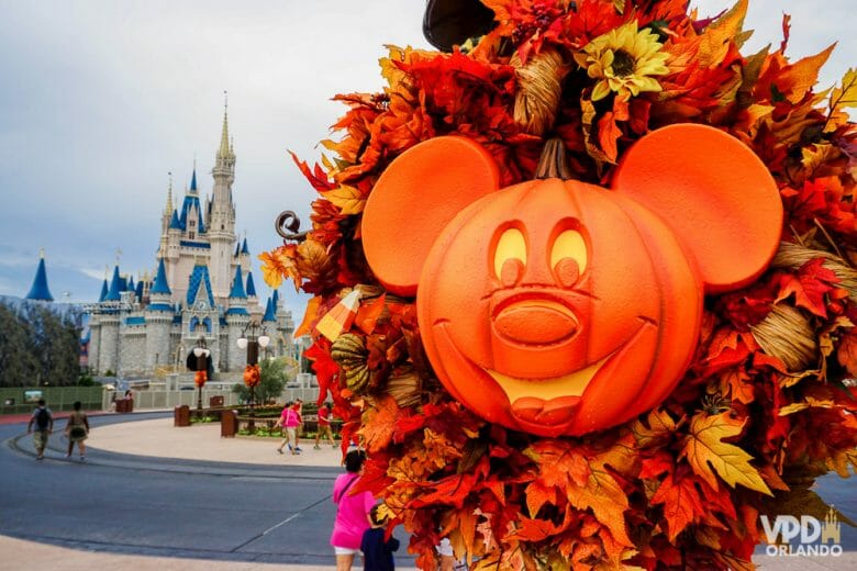 Foto da decoração de Halloween da festa do Magic Kingdom, uma abóbora em formato de Mickey iluminada por dentro. O castelo da Cinderela é visível ao fundo da foto, assim como alguns visitantes.