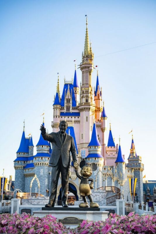 Foto publicada pela Disney do castelo da Cinderela do Magic Kingdom após a reforma, com as torres pintadas em um azul mais vibrante e novos detalhes em dourado. É possível ver a estátua de Walt Disney de mãos dadas com o Mickey e o castelo ao fundo. 