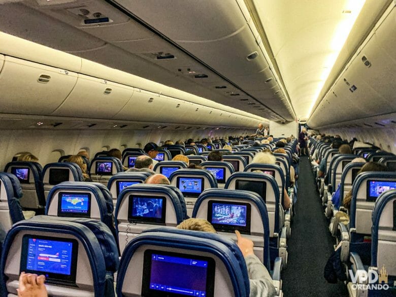 Não dá pra saber ainda quando as fronteiras serão reabertas. Imagem do interior de um avião. É possível ver a parte de trás de diversas fileiras de poltronas, com as telas acopladas atrás.