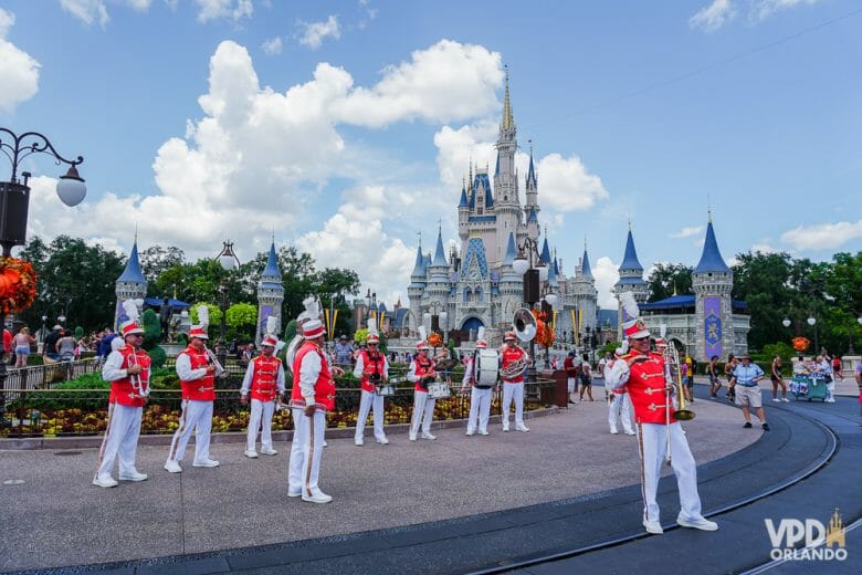 Imagem do Magic Kingdom durante o dia, com a banda que se apresenta na Main Street em suas roupas vermelhas e brancas e o castelo da Cinderela ao fundo. 