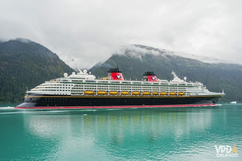 Foto do navio de cruzeiro da Disney em alto mar, com montanhas ao fundo 