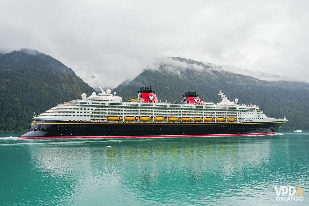 Foto do navio de cruzeiro da Disney em alto mar, com montanhas ao fundo