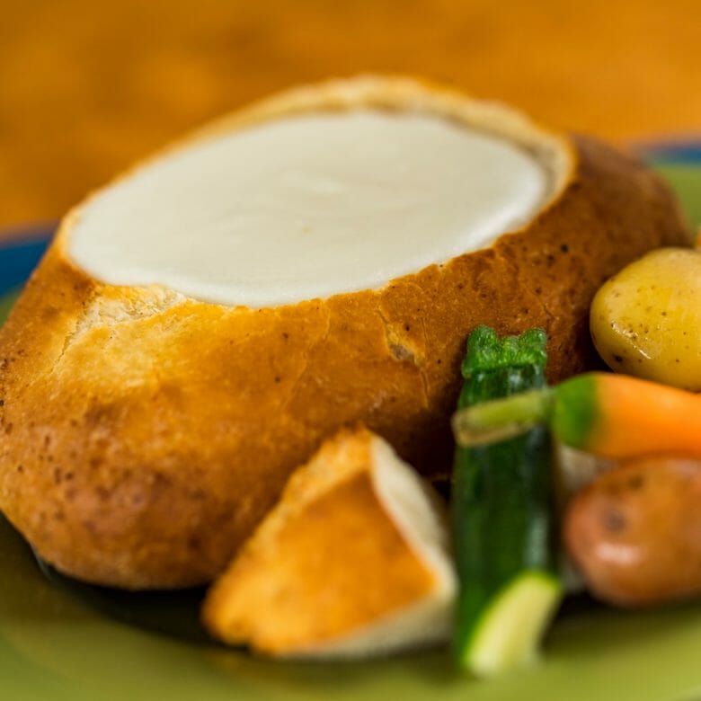 Imagem de uma sopa dentro de um pão, com alguns vegetais do lado direito.