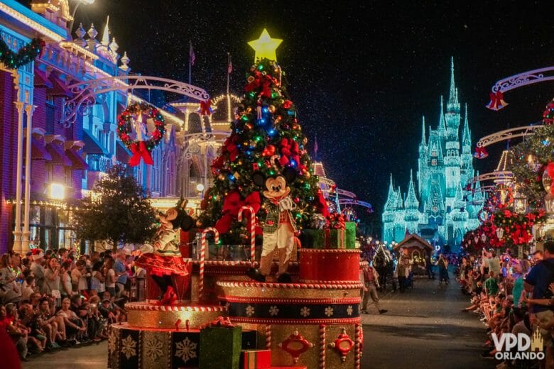 Parada de Natal do Magic Kingdom com Mickey em carro alegórico e castelo iluminado com luzes de Natal ao fundo. A semana do natal é uma das épocas para evitar visitar os parques por causa da lotação.