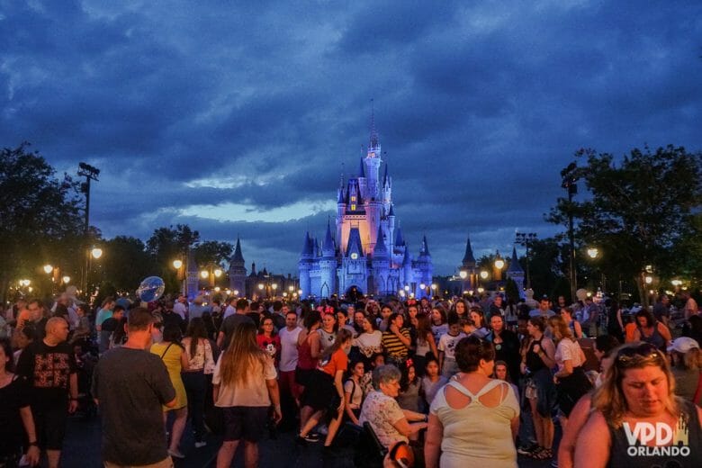 Imagem do Magic Kingdom à noite. A foto mostra o castelo iluminado de roxo e muitas pessoas em frente.