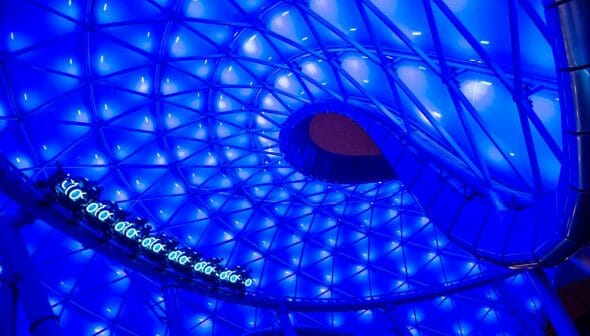 Foto da montanha-russa baseada no filme Tron, que vai abrir no Magic Kingdom. Ela é iluminada por luzes azuis e também tem um fundo azul.