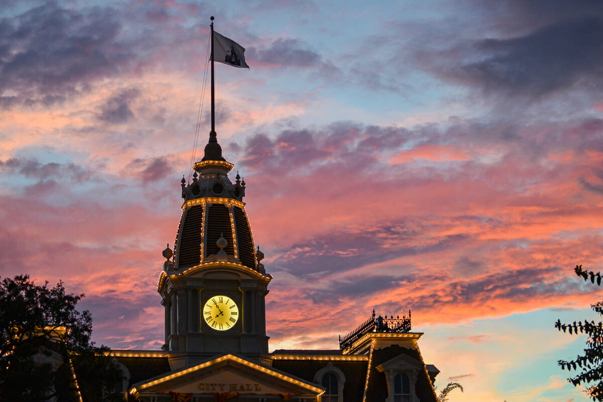 Imagem do topo do City Hall no Magic Kingdom durante o pôr do sol. Há uma bandeira com um desenho do castelo.