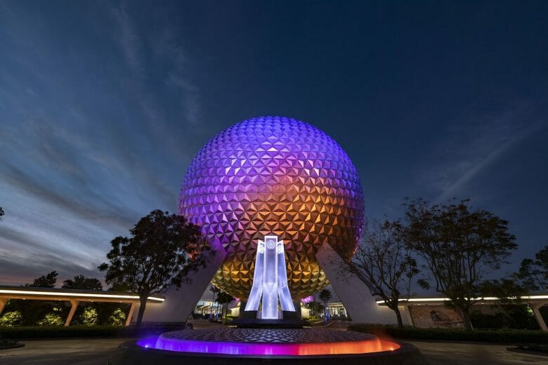 Imagem da nova fonte na entrada do Epcot durante à noite. A Spaceship Earth e a fonte estão iluminadas de roxo, rosa e laranja.