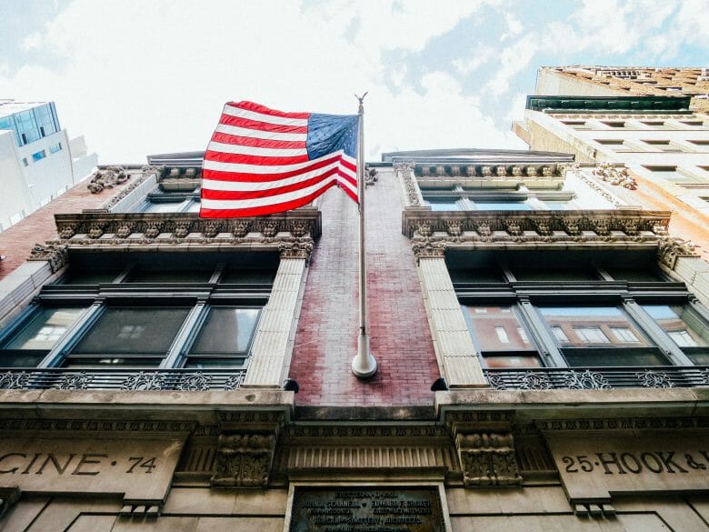 Foto de um prédio com uma bandeira dos Estados Unidos e o céu claro acima.
