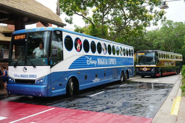 Imagem de dois ônibus estacionados. O que está na frente é azul e branco, traz personagens da Disney e o texto Magical Express.