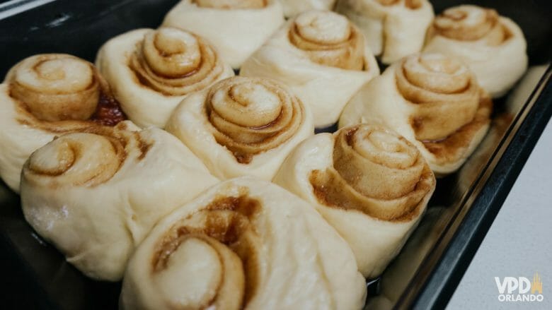 Imagem de 12 cinnamon rolls ainda crus crescendo em uma assadeira.