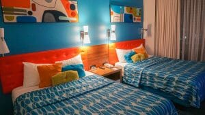 Imagem de duas camas no hotel Cabana Bay. A cabeceira é laranja, a parede é azul e as camas tem colchas azuis e almofadas coloridas.