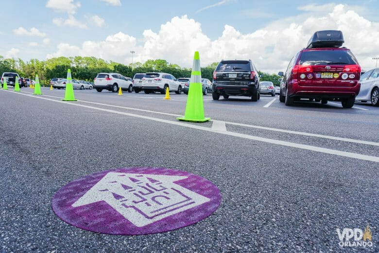 Imagem de carros de várias cores estacionados. Há cones verdes e um círculo roxo no chão indicando o caminho do Magic Kingdom.