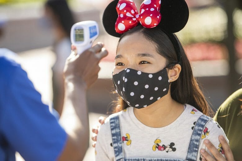 A Disney voltou a exigir o uso de máscaras em áreas internas. Uma menina tem a sua temperatura checada e usa uma máscara preta do Mickey.