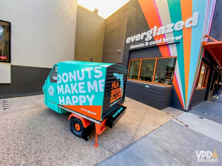 Entrada da Everglazed Donuts. A parede é preta com riscos coloridos. Há um caminhãozinho de entrega estacionado. 