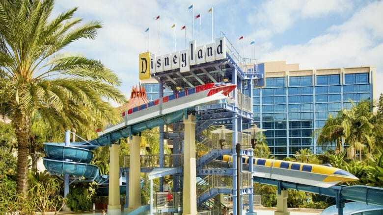 Imagem do Disneyland Hotel, com a torre de janelas espelhadas ao fundo e o logo do complexo na frente.