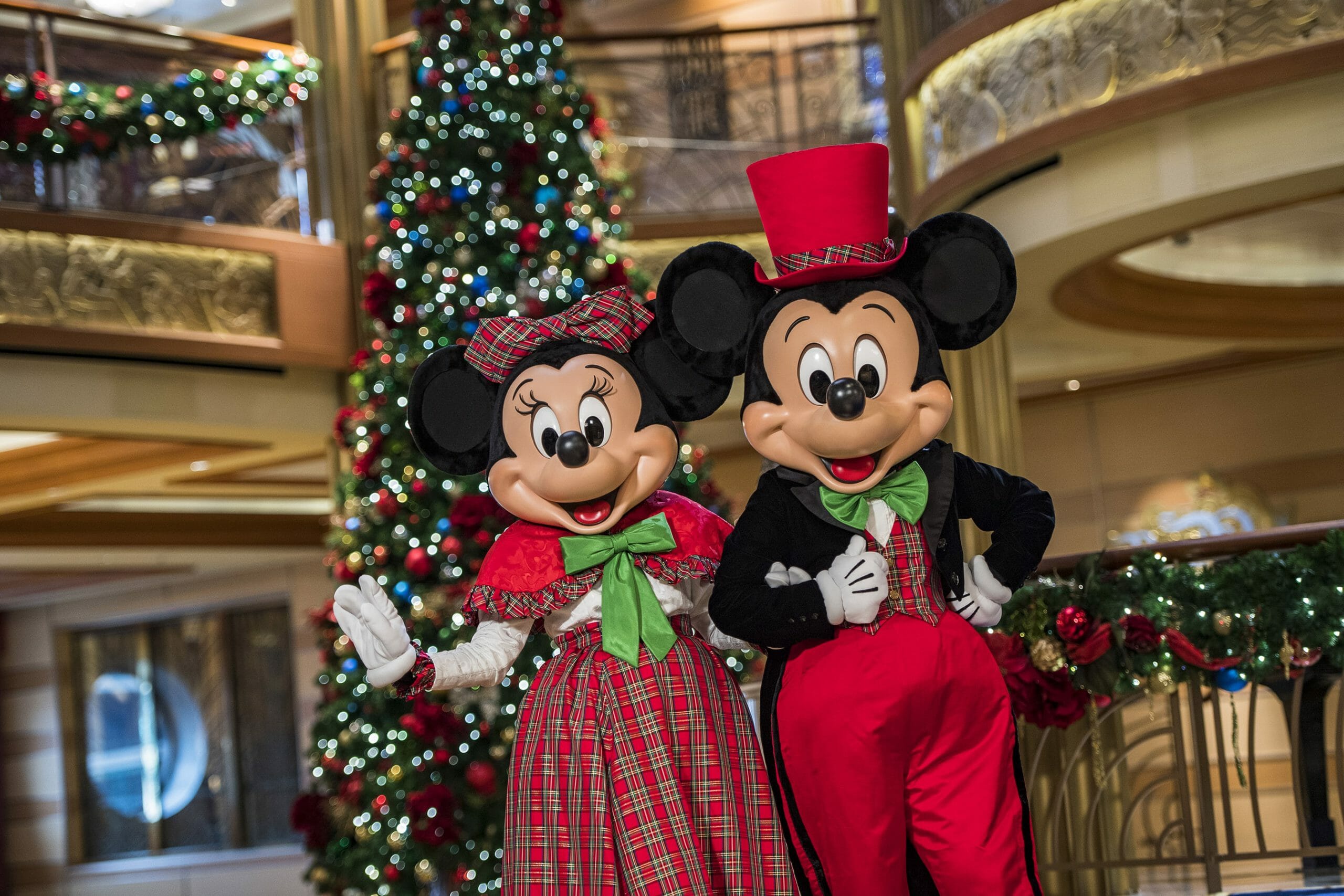 Mickey e Minnie com roupas de Natal em frente a uma árvore de Natal no átrio do navio de cruzeiro da Disney