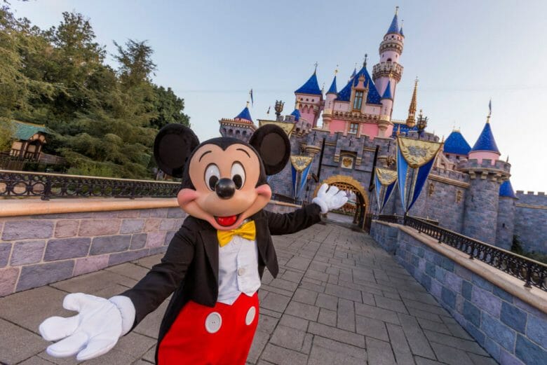 Mickey de roupa clássica e braços abertos em frente ao castelo da Disneyland California